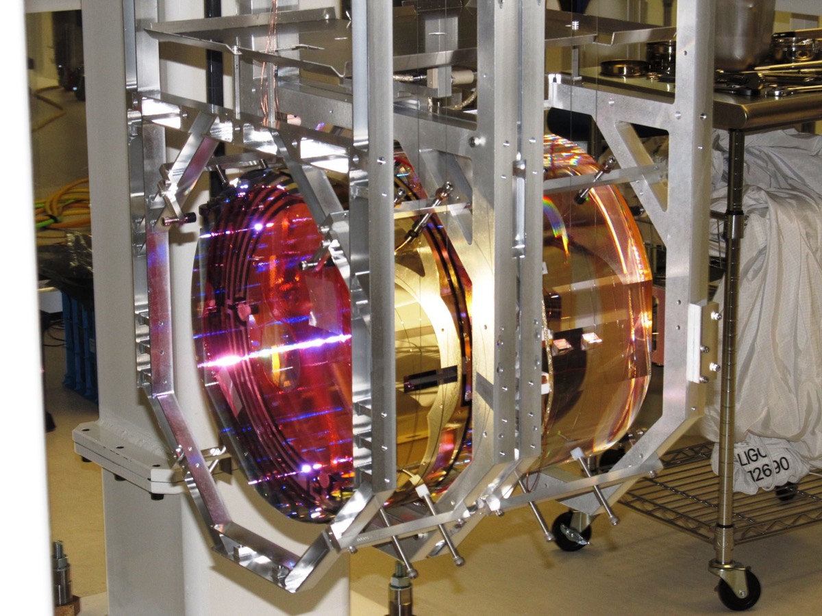 LIGO test mass mirror suspended by glass fibers, dramatically lit in red and gold
